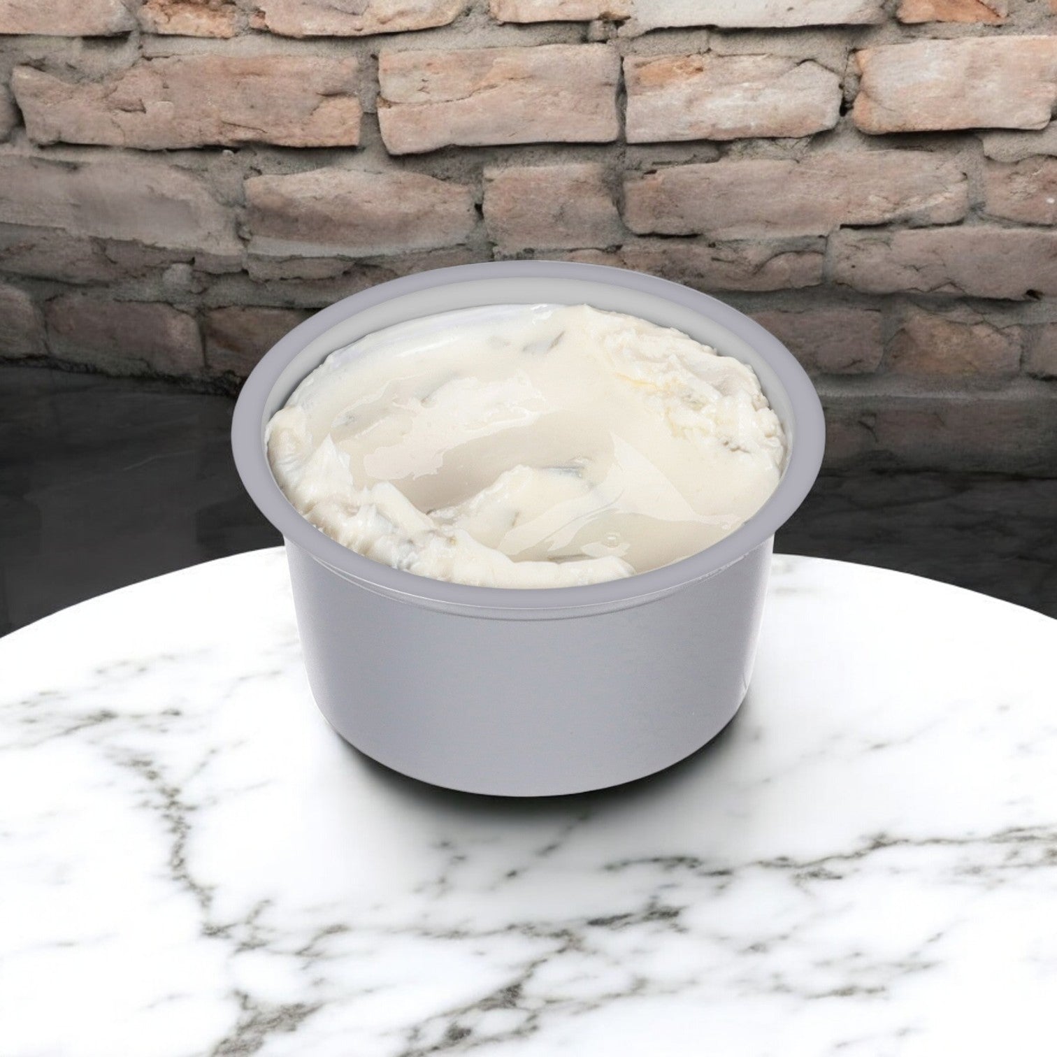 A Philadelphia Cream Cheese Chive & Onion spread cup sits on a marble surface, its charm enhanced by the brick wall backdrop, exuding the classic allure akin to Philadelphia Cream Cheese.