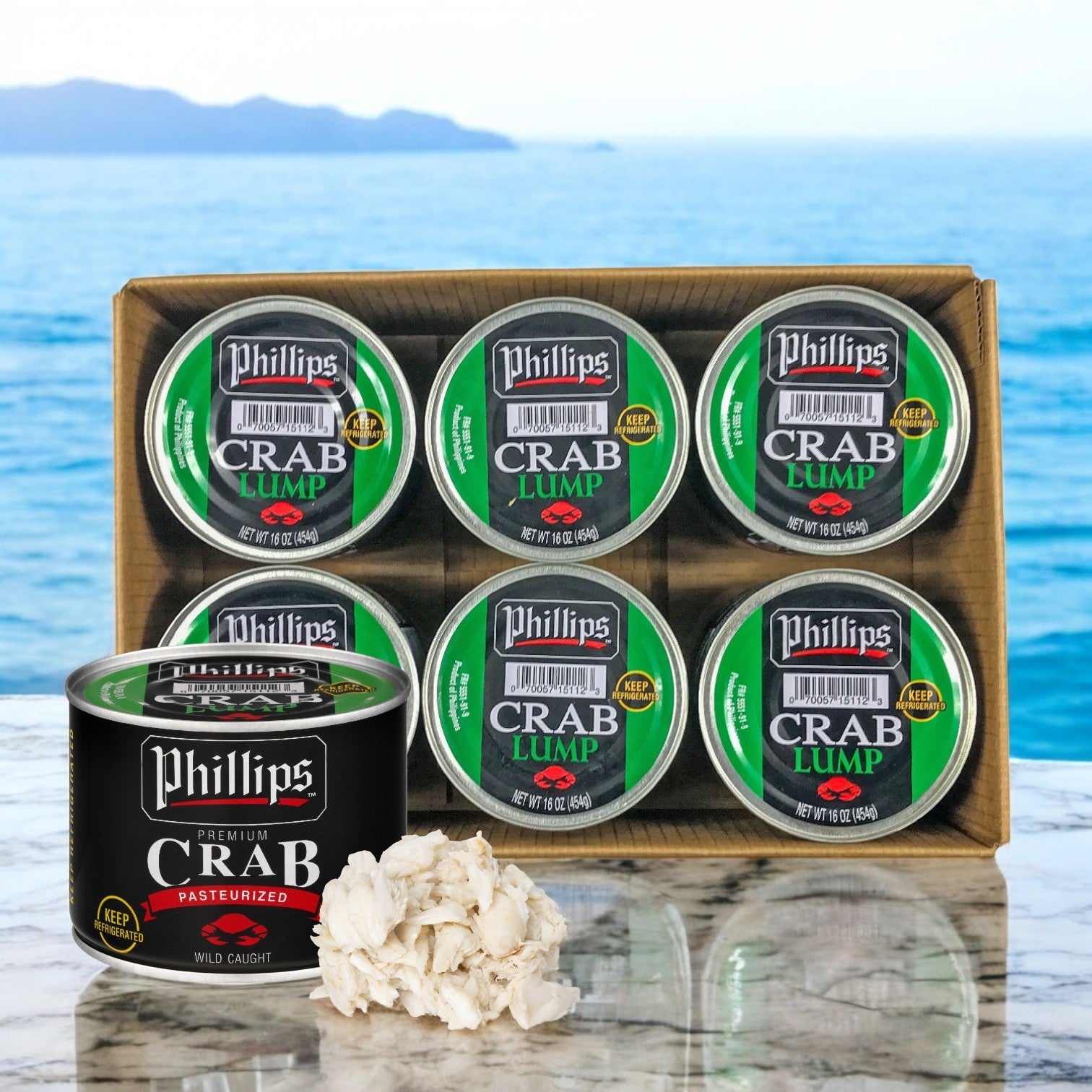Six cans labeled "Phillip Foods, 6 Crab Meat Lump Pasteurized Southeast Asia Pack- 6 Pounds" sit on a marble surface beside a pile of lump crab meat, with the ocean in the background. Ideal for seafood dishes.
