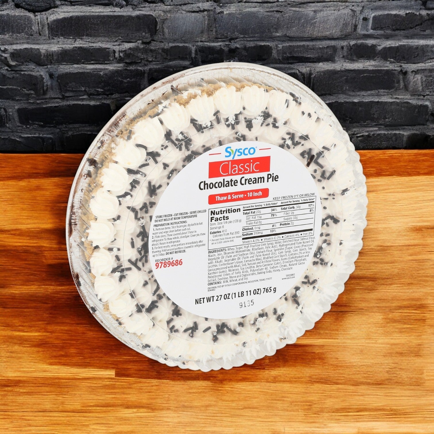 A 10" Sysco Classic Chocolate Cream Pie, featuring a rich chocolate filling and whipped cream topping, rests on a wooden surface against a brick wall. It's ideal for fans of thaw & serve convenience.