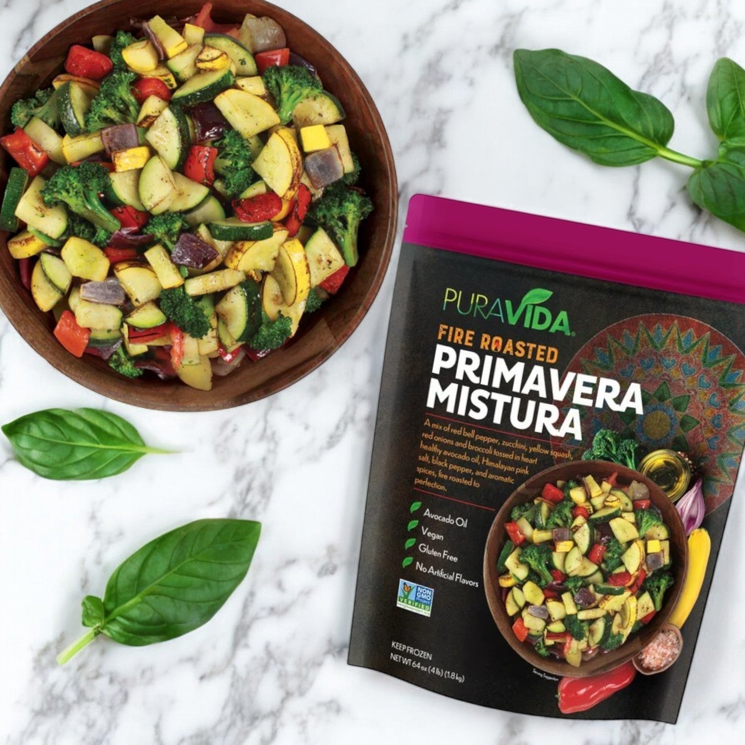A bowl of mixed vegetables with fire-roasted Brussels sprouts is next to a package labeled "PuraVida Fire Roasted Primavera Mistura, 64 oz." by Pura Vidaa on a marble surface with fresh basil leaves.
