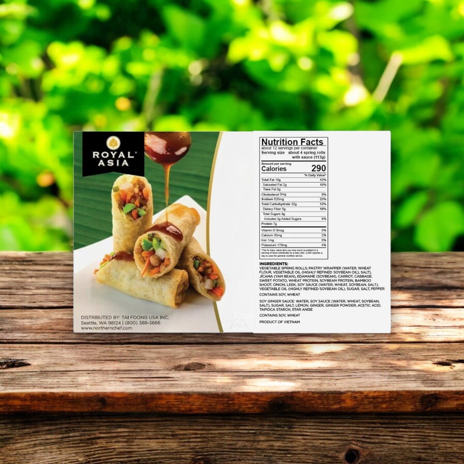 A 50-count box of Royal Asia Vegetable Spring Rolls by Bibigo features crispy, vegetarian-friendly rolls filled with vegetables and soy ginger sauce, all presented against a lush green leafy background on a wooden surface.