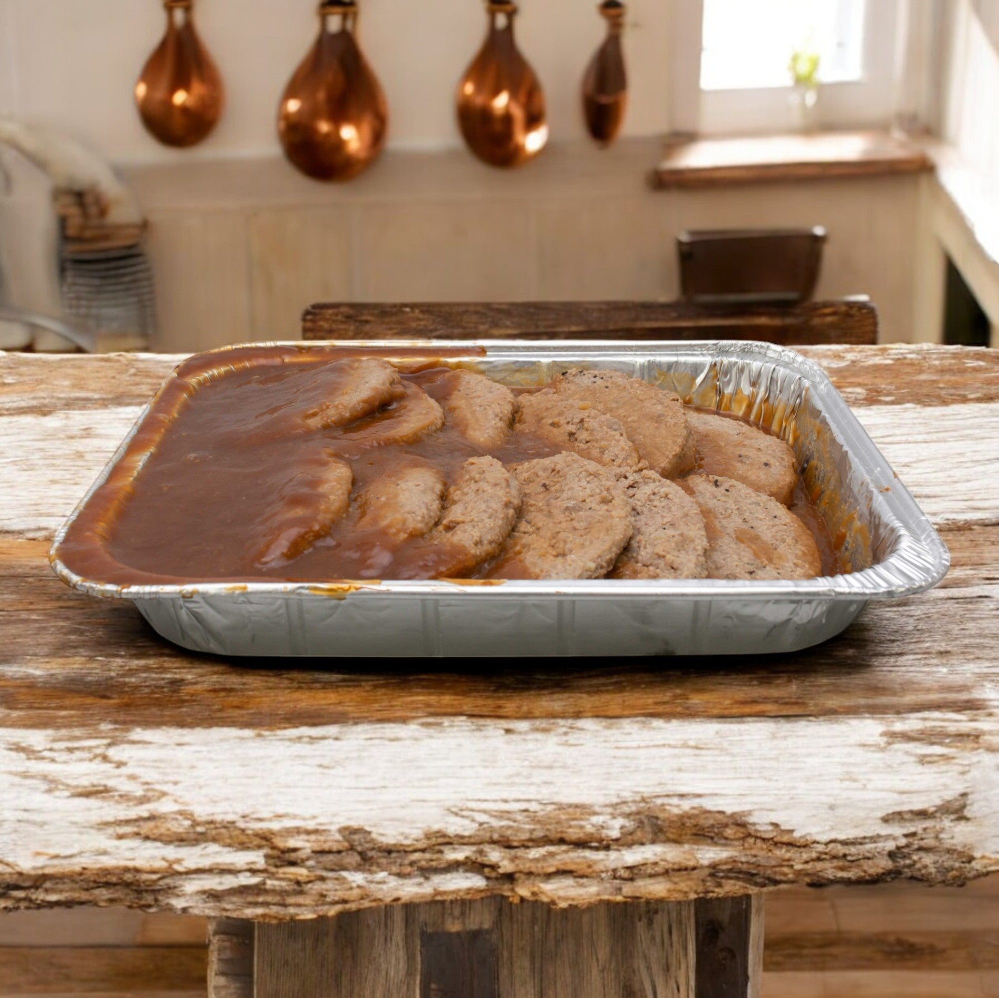 A 69 oz. tray of Stouffer's Salisbury Steak with Gravy is placed on a rustic wooden table in a cozy kitchen, with copper pots hanging in the background, hinting at quality ingredients used throughout.