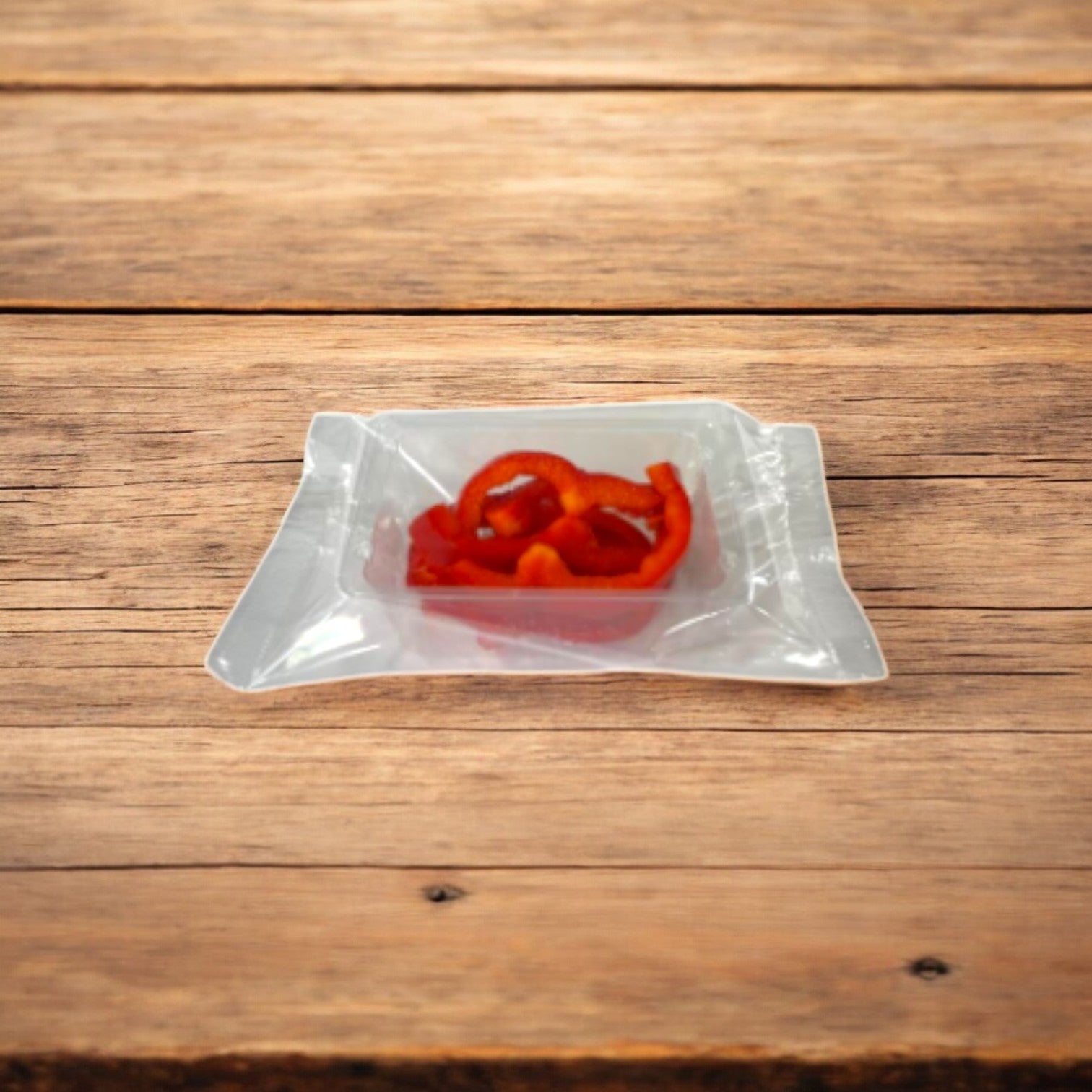 An Easy Lunches vacuum-sealed package of Sliced Red Peppers, available in a 2.5 oz size from a 100-pack, rests on a wooden surface, displaying their vibrant flavor and color. Made to order with a 7-day shelf life upon receipt.