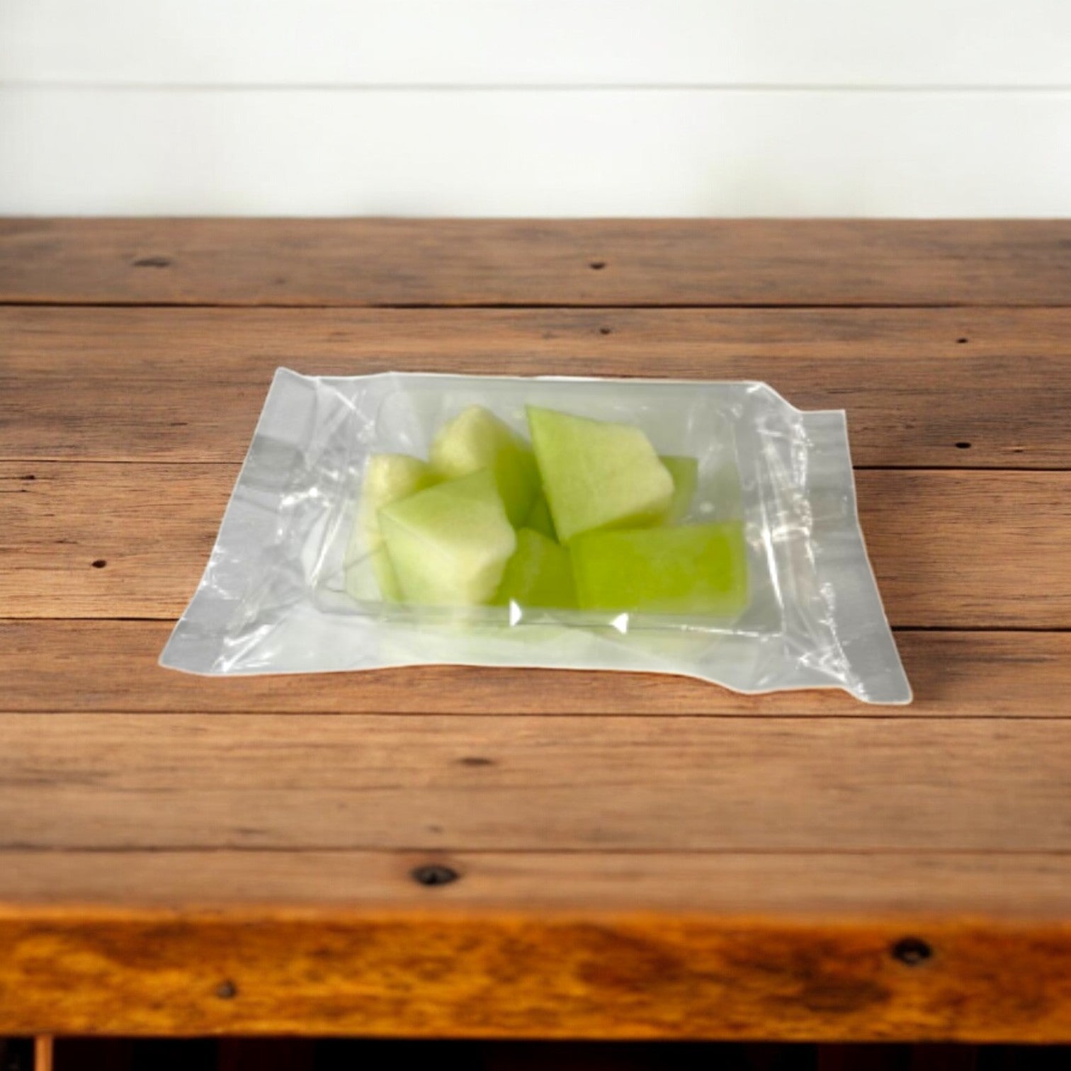 Easy Lunches' Honeydew Melon Chunks, in a vacuum-sealed bag on a wooden surface, display their refreshing taste and vibrant green and white hues. Each 2.5 oz. pack is made to order with a 7-day shelf life after delivery.