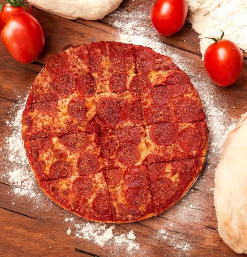 A Labriola Chicago Thin Crust Pepperoni Pizza from the 3 Count Combo sits on a wooden surface, surrounded by fresh tomatoes, dough, and scattered flour.