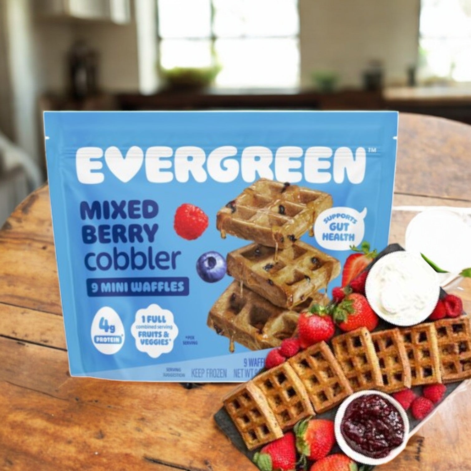 A package of Evergreen Mini Waffles, Mixed Berry Cobbler-9 Oz, sits on the table surrounded by strawberries, blueberries, additional waffles, and a jam bowl—creating a festive holiday breakfast scene.