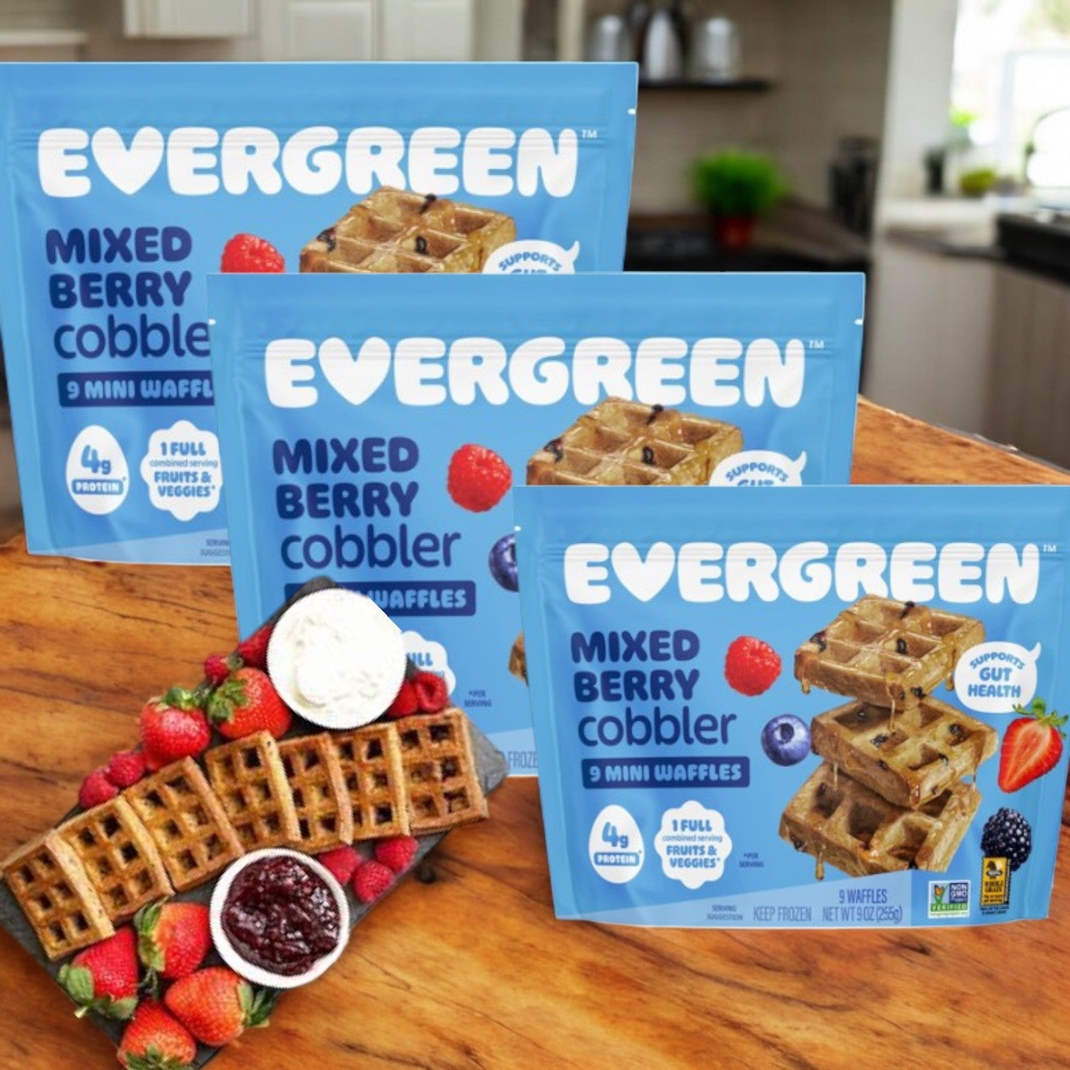 Three Evergreen Mini Waffles (Mixed Berry Cobbler-9 Oz, 3 Count) lie on a kitchen counter with fresh berries and other waffles, making a festive holiday breakfast treat.