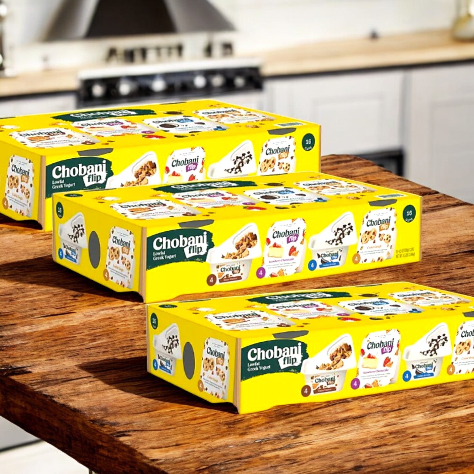 On a wooden kitchen table, three cases of Chobani Flip Lowfat Greek Yogurt Variety Pack, 4.5 oz, 16 count are displayed, showcasing a delightful array of flavors.
