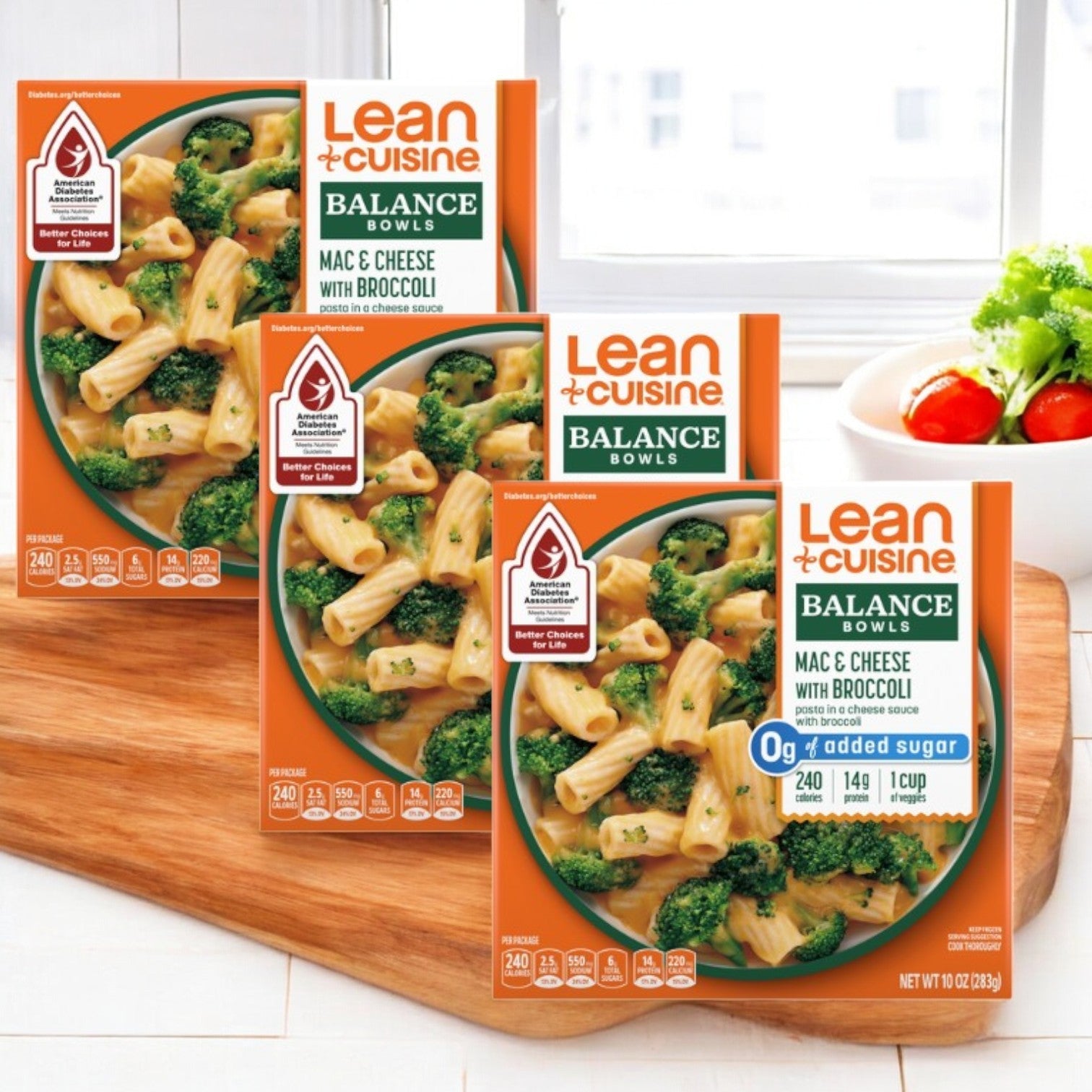 Three Lean Cuisine Mac & Cheese Broccoli Bowls are displayed on a wooden cutting board as a convenient frozen meal option, with a small bowl of red tomatoes in the background adding a pop of color.