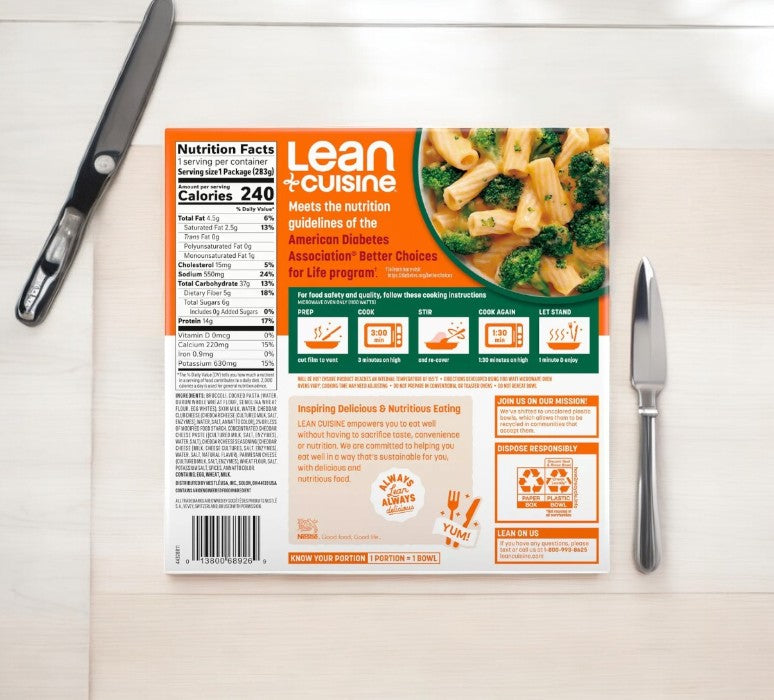 A Lean Cuisine Mac & Cheese Broccoli Bowl-10 Oz-1 Count rests on a table, displaying nutrition facts and cooking instructions, with a knife and fork neatly positioned beside it.