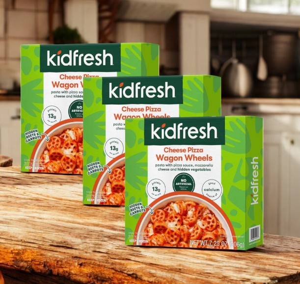 Three boxes of KidFresh Wagon Wheels Cheese Pizza, each 7.25 oz, are displayed on a wooden surface in a cozy kitchen setting, featuring an organic whole wheat crust and hidden vegetables for a healthy take on the classic favorite.