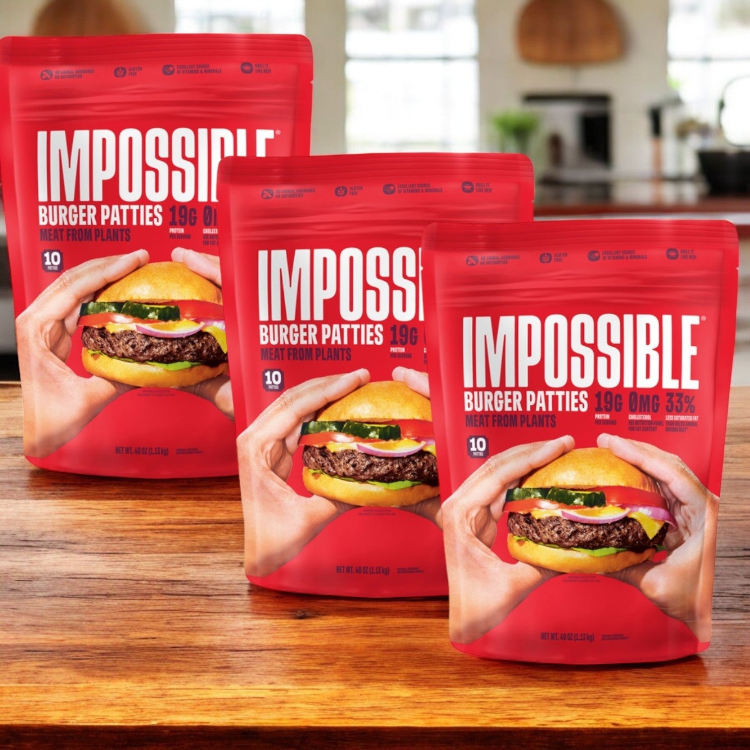 Three packs of Impossible Burger Patties Made From Plants by Impossible Foods are on a wooden surface. The red packaging showcases a burger image and highlights the soy protein-rich, plant-based ingredients and protein content.