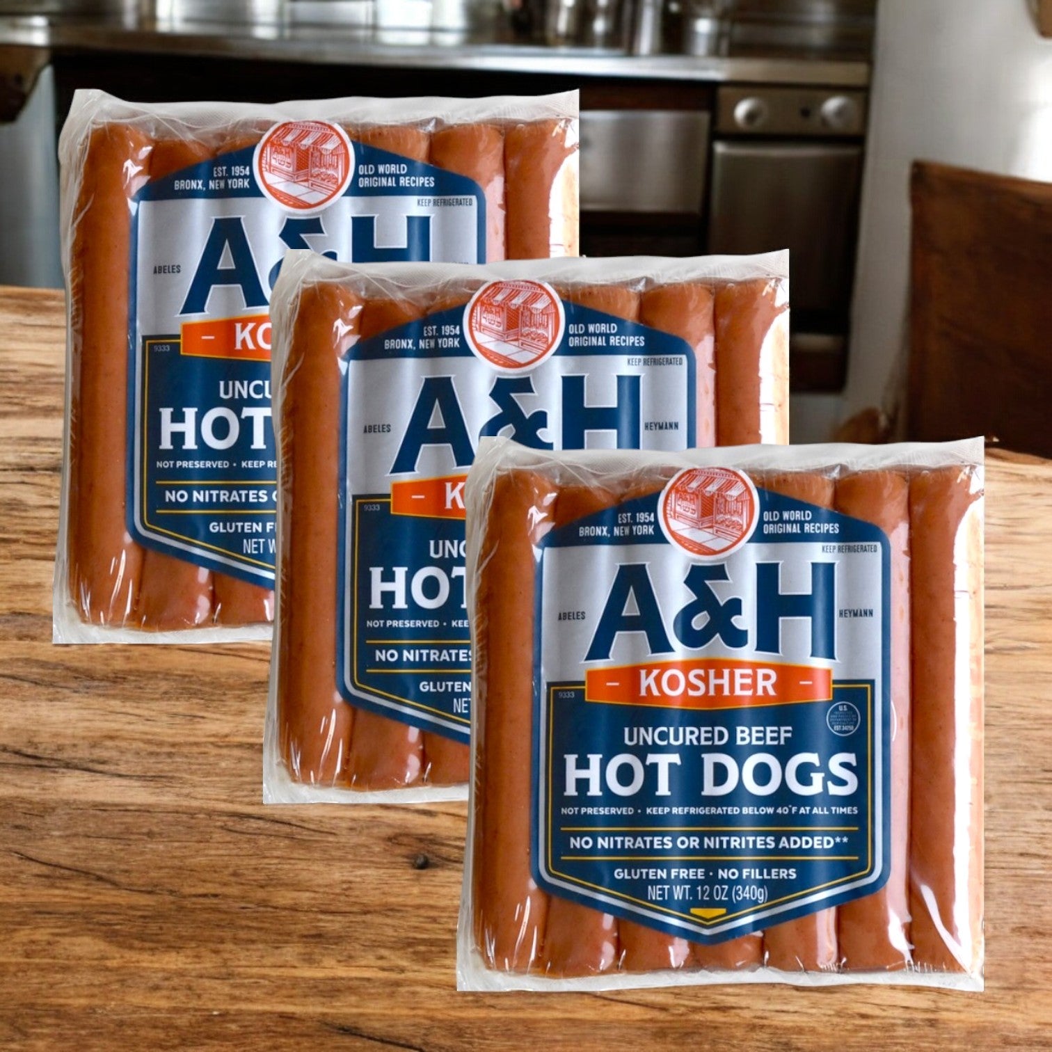 Three packs of A&H Meats' 14 oz All Beef Kosher Hot Dogs are set on a wooden surface, each labeled gluten-free and free from added nitrates or nitrites, offering a pure and savory option for your meal.