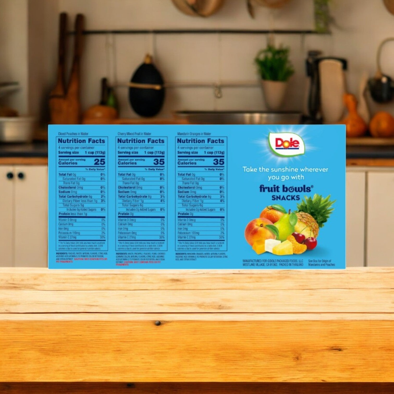 A box of Dole Fruit Bowls Snack, Variety Pack (12 Count) is on the kitchen counter, displaying vibrant fruit images and nutrition facts. This healthy snack from Dole is ideal for any time of day.