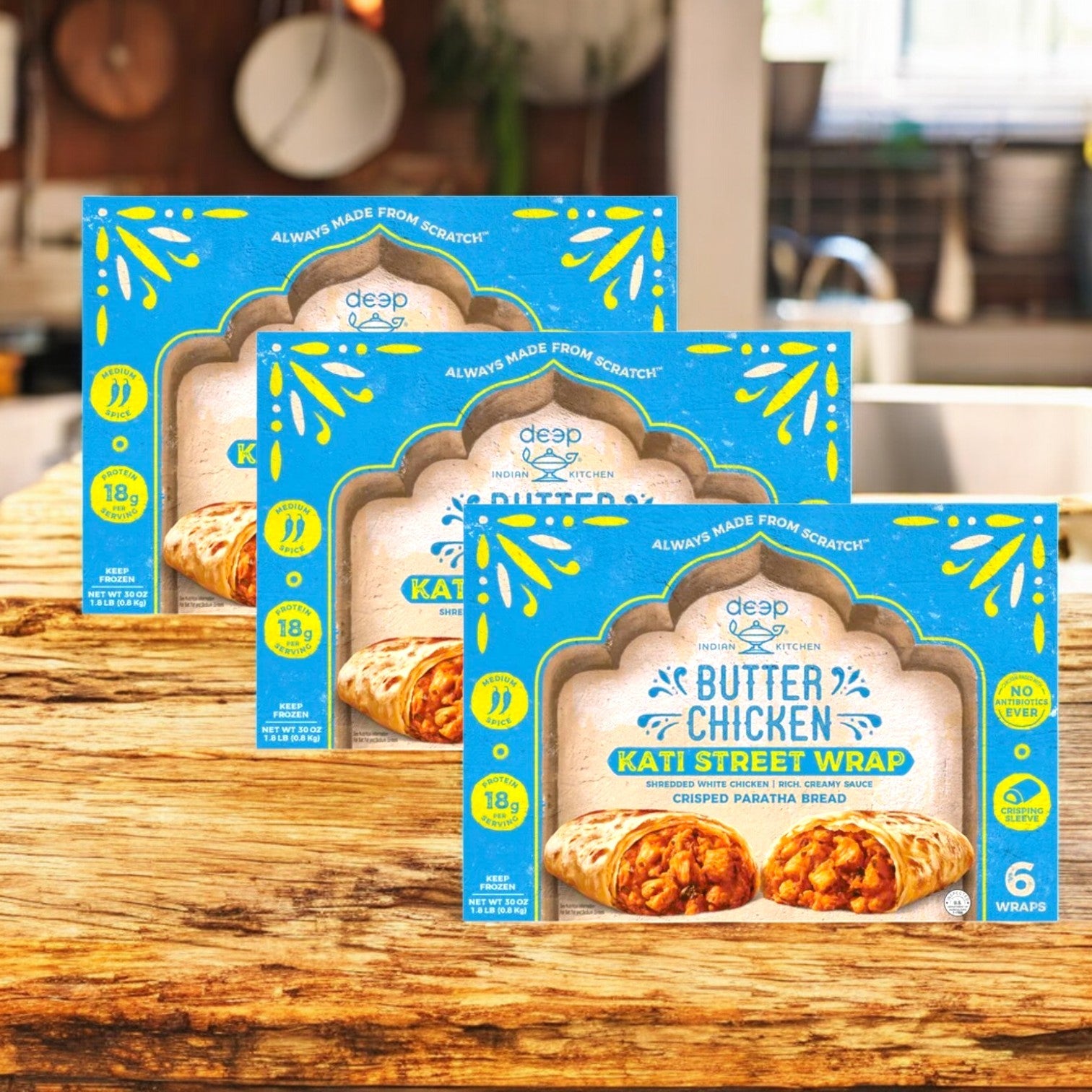 Three cases of Deep Indian Kitchen Kati Street Wrap, Butter Chicken (6 count each) from Deep Indian Kitchen are displayed on a wooden surface, offering a tasty and convenient Frozen Indian Meal option.