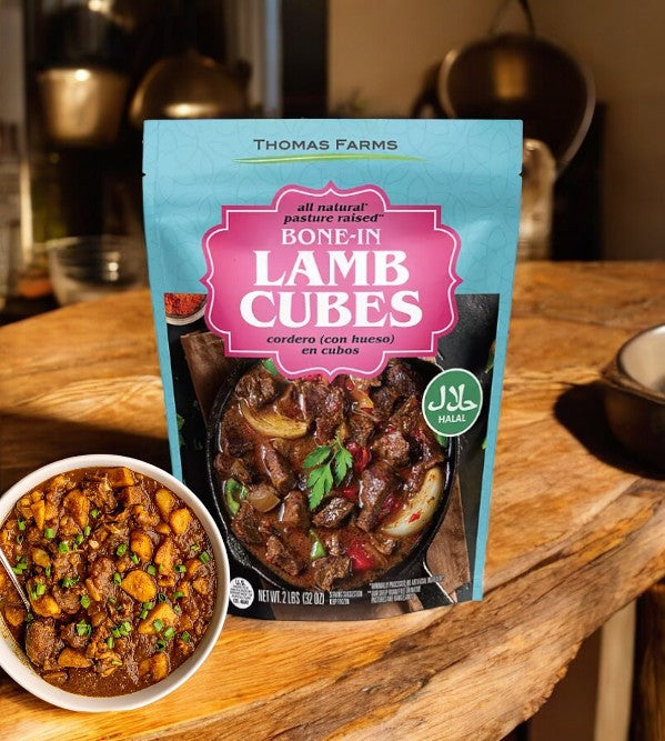 A pack of Thomas Farms Australian Bone In Lamb Cubes, Frozen, 2 lbs., is displayed on a wooden surface beside a bowl of cooked lamb stew.