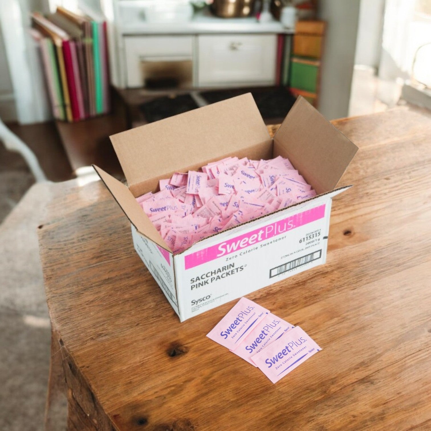 An open box of Sysco Sugar Substitute Packet Pink (1g, 2000 count) sits on a kitchen table, with loose packets nearby. This popular low-calorie sweetener is ideal for drinks and recipes.