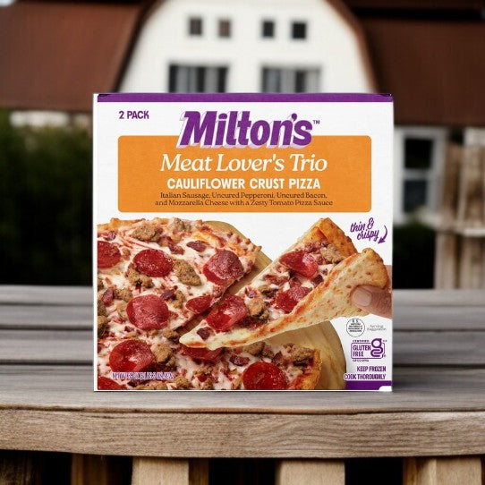 A box of Milton's Meat Lover's Cauliflower Crust Pizza, 17.5 oz, 2-count, sits on a wooden surface with a barn and greenery in the background—highlighting this gluten-free frozen pizza from Milton's.