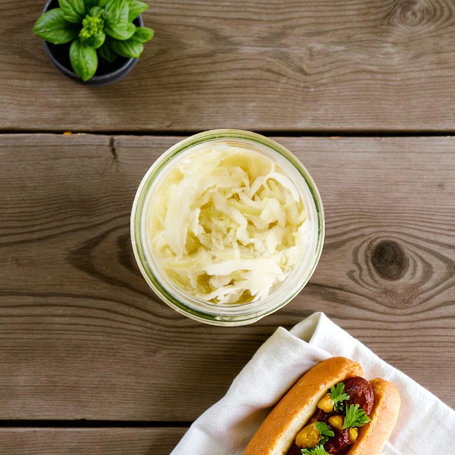 A 32 oz jar of Vienna Beef Sauerkraut sits on a wooden table, with a potted plant above and a topped hot dog on a napkin below.