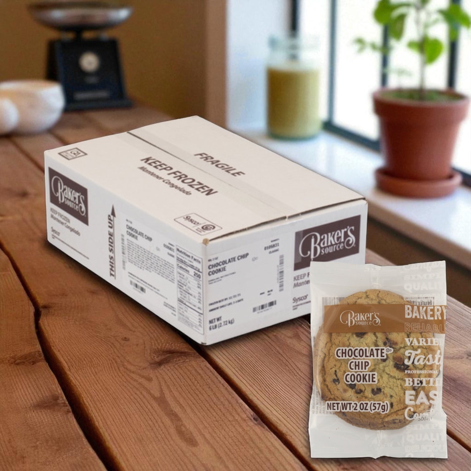 A box of Baker's Source Classic Cookie Chocolate Chip Individually Wrapped 2 Ounce - 48 Count sits on a wooden table; in front, an individually wrapped cookie showcases the convenience and appeal of these treats.