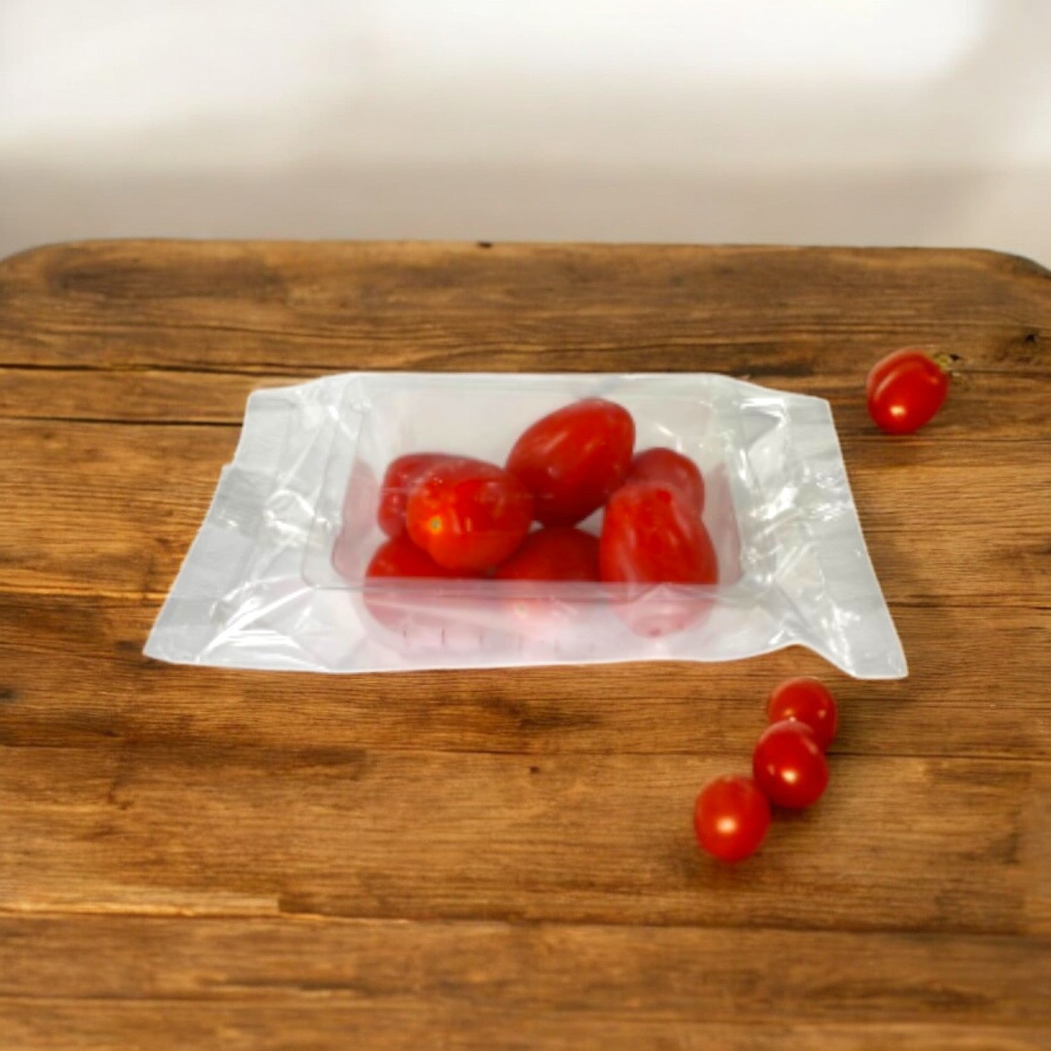 Easy Lunches Grape Tomatoes, 2.5 oz., are displayed in a sealed tray on a wooden surface, accompanied by sweet tomatoes scattered beside it.