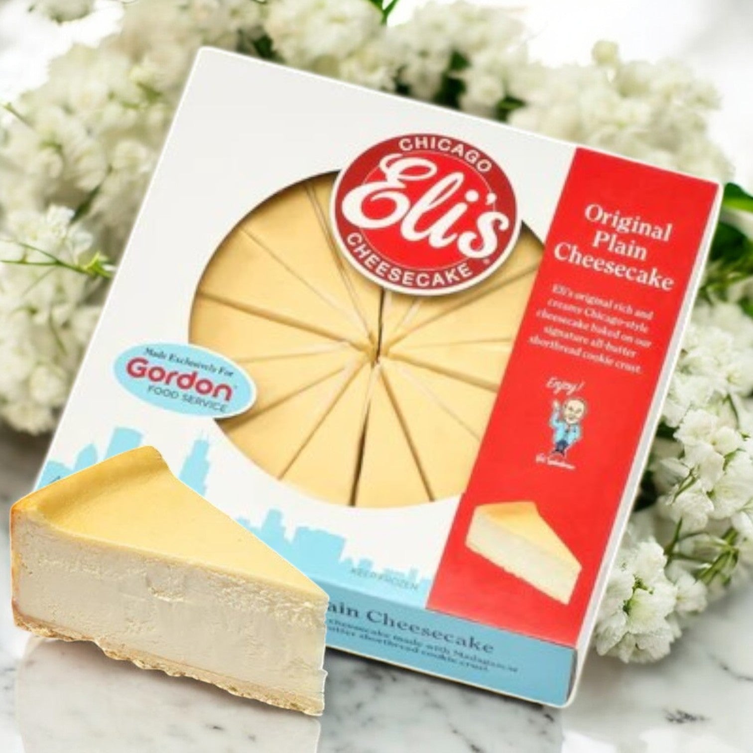 Displayed is a box of Eli's Cheesecake 9" Original Plain Cheesecake with pre-sliced convenience and a buttery shortbread crust, accompanied by a slice, set against white flowers.