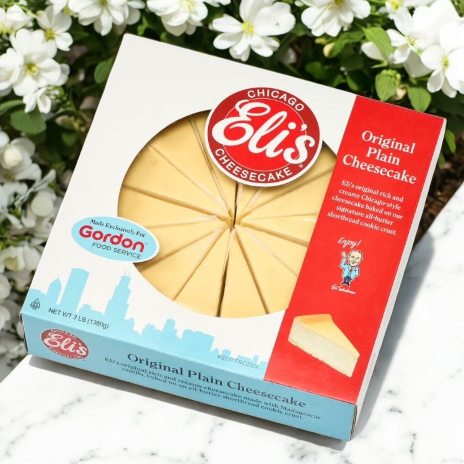 A box of Eli's 9" Original Plain Cheesecake- 3 Count by Eli's Cheesecake reveals slices with white flowers, highlighting its buttery shortbread cookie crust.