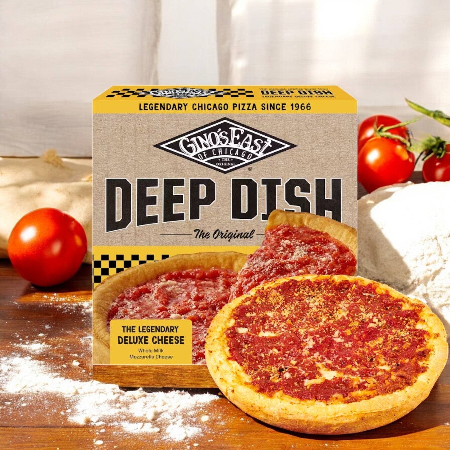 A box of Gino's East Pizza, Deluxe Cheese, Deep Dish-1 Count rests on a wooden surface amid fresh tomatoes and dough, offering an authentic deep-dish experience.