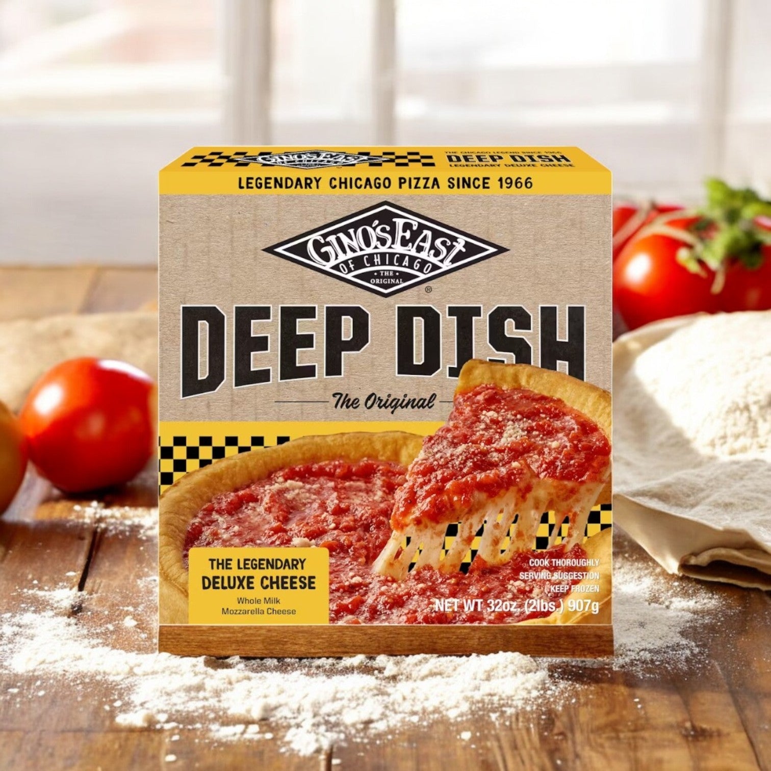 A Gino's East Pizza Deluxe Cheese Deep Dish sits on a wooden table surrounded by fresh tomatoes, dough, and flour, with the rich aroma of mozzarella cheese wafting through the air.