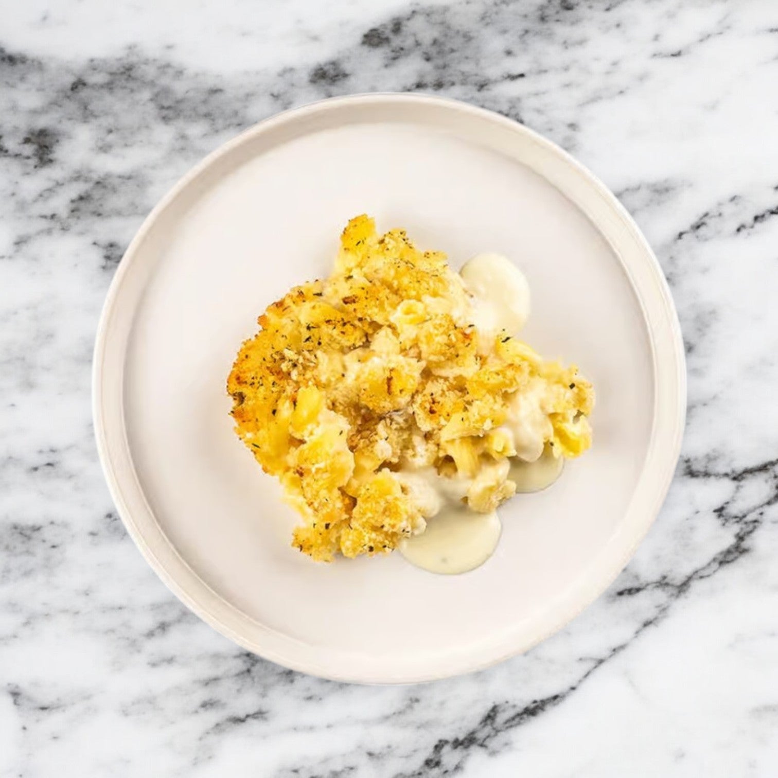 FoodHaul's Rick's Mac & Cheese Vegan, served on a white dish over marble, offers plant-based comfort with its crispy golden top and rich, dairy-free cheese sauce that melts delightfully in every bite.
