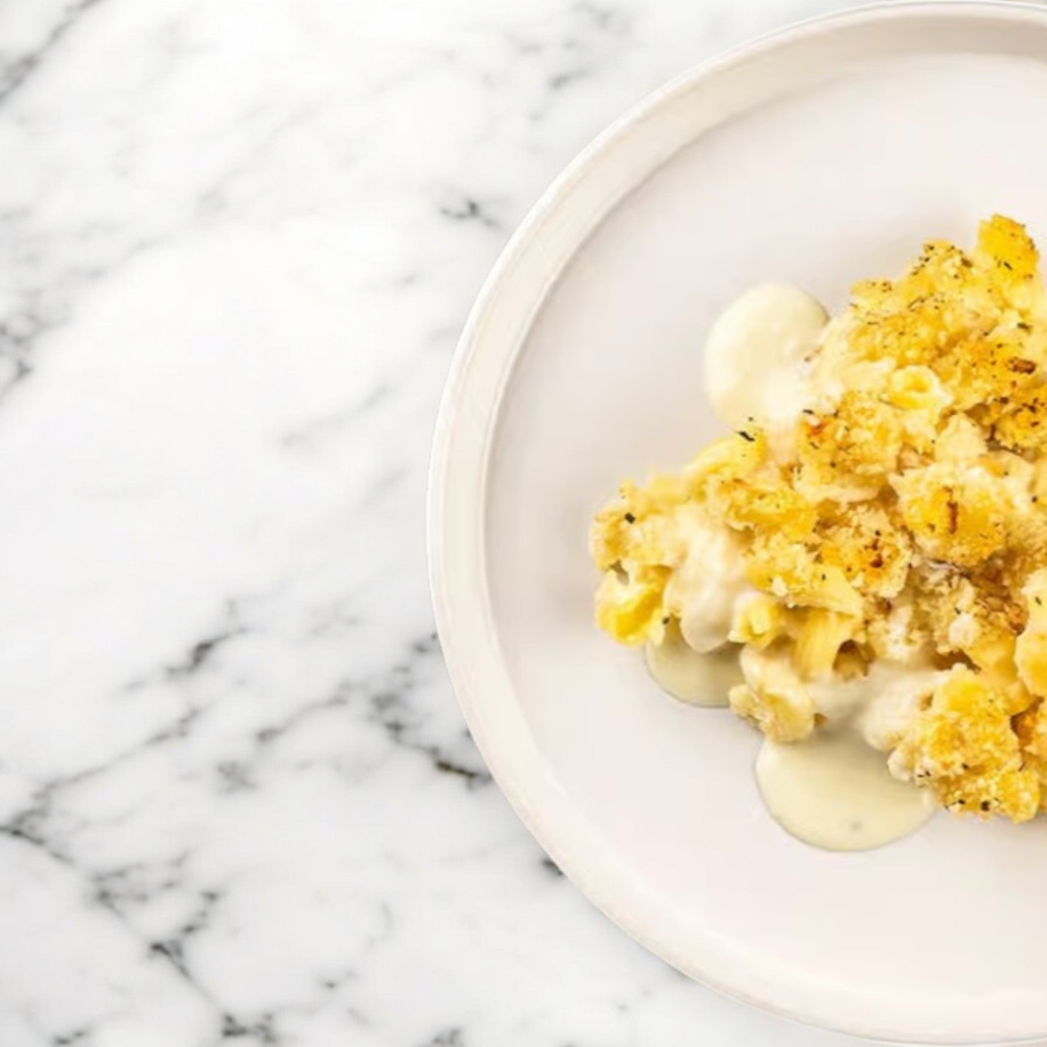 A white plate on a marble surface holds Rick's Mac & Cheese Vegan by FoodHaul, featuring creamy pasta with a golden crust. This delightful dish is a plant-based comfort food favorite with its rich, dairy-free cheese sauce.