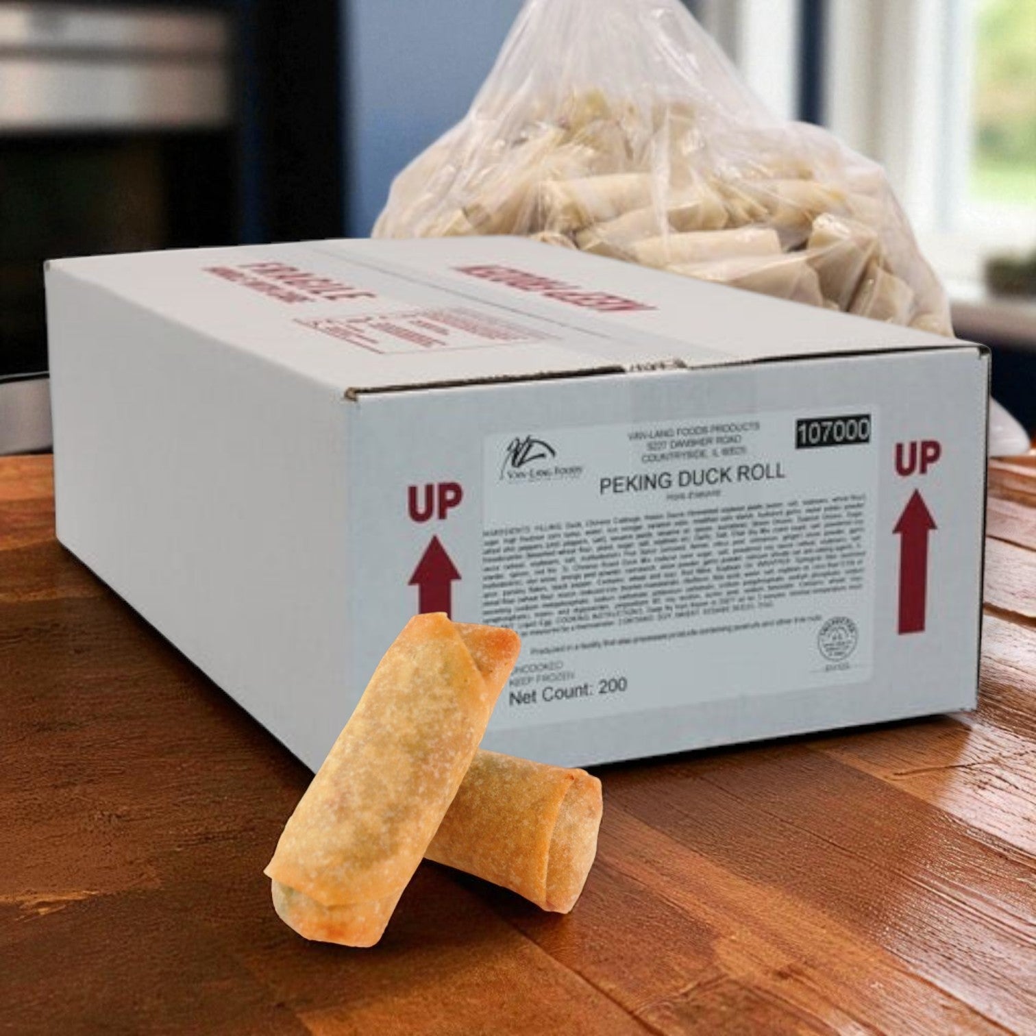 A white box labeled “Van Lang Brie & Raspberry Phyllo Bites – 200 Count (4 Trays of 50, Frozen Appetizers)” sits on a wooden counter with phyllo bites in front, creating an elegant appetizer display perfect for catering events.