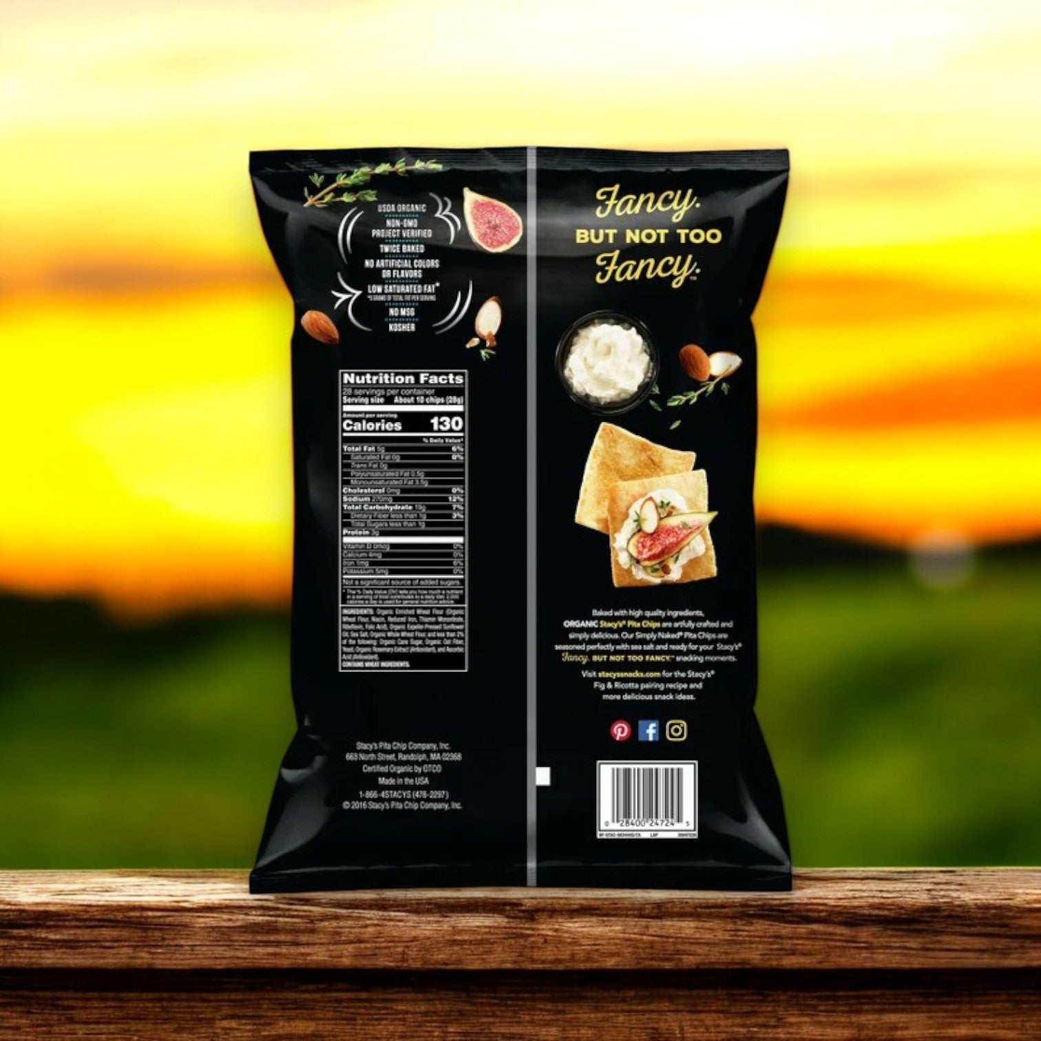 The back of a Stacy's Organic Simply Naked Pita Chips 28 oz. bag shows nutritional facts, ingredients, a serving suggestion image with text "Fancy, but not too fancy." Enjoy these non-GMO treats for pure snack perfection against a blurry outdoor backdrop.