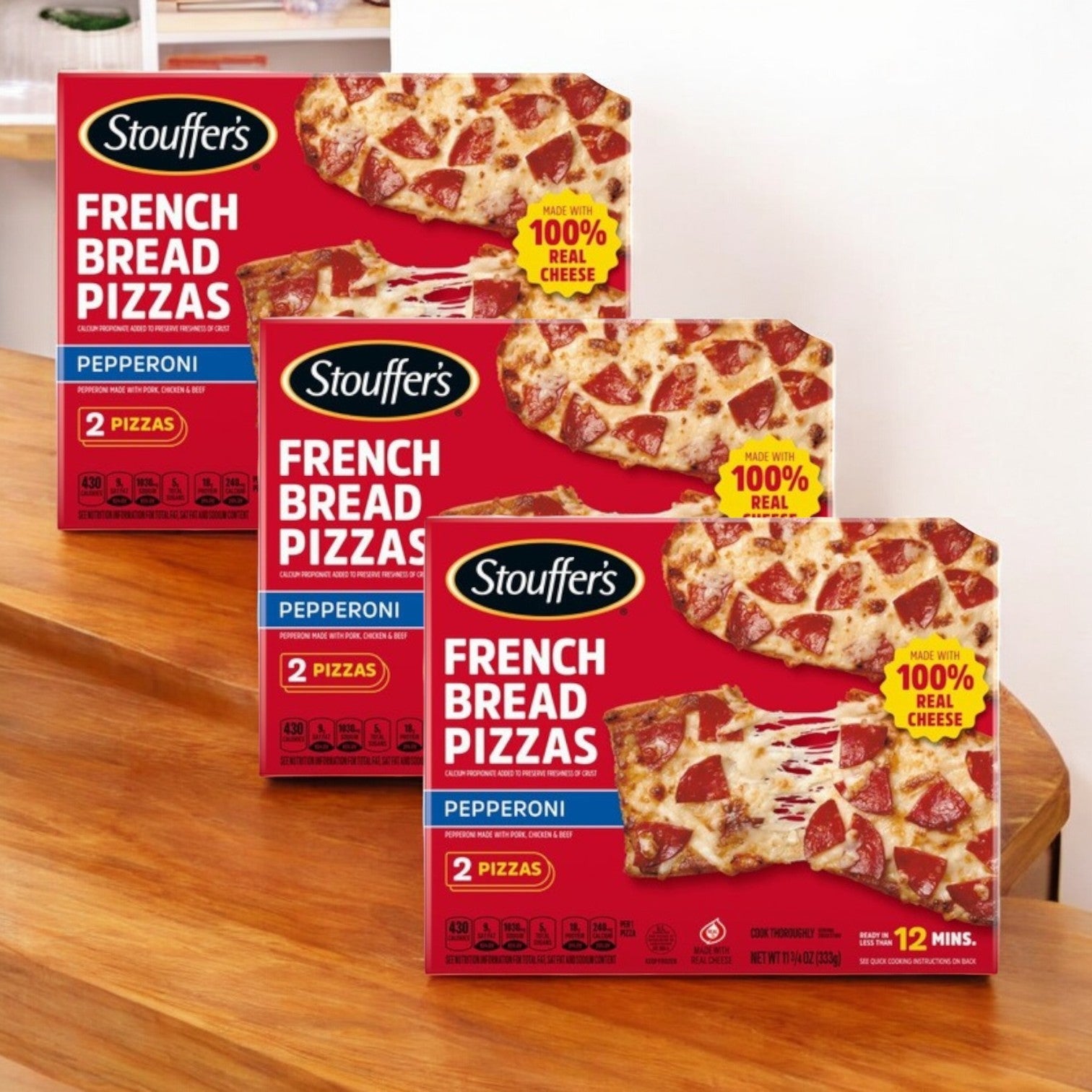 Three boxes of Stouffer's Deluxe French Bread Frozen Pizza, topped with rich mozzarella cheese, are displayed on a wooden table.