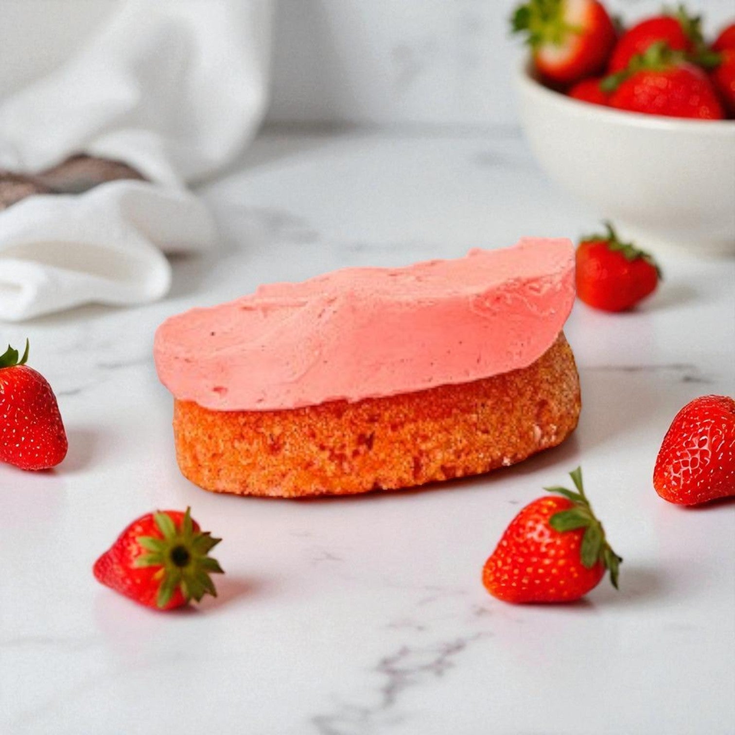 The Eat Cup Cake Strawberry Short Cake Cup with Spoon (2.5 oz) by Eat Cup Cake sits on a white surface topped with pink frosting, surrounded by fresh strawberries, with a bowl of strawberries in the background.