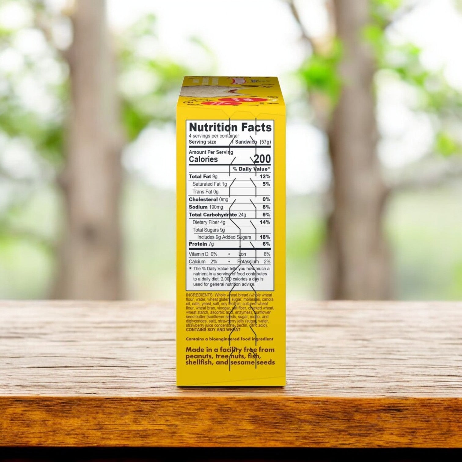 A SunButter Sunflower Butter & Strawberry Jelly Sandwich Jammies box, with nutritional facts and 200 calories per serving, rests on a wooden table against a blurred green backdrop. This nut-free delight offers health and convenience in each bite.