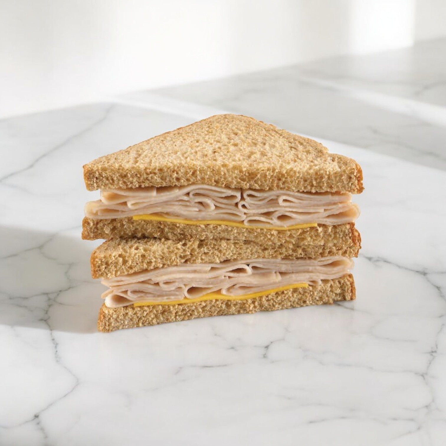 The E.A. Sween Oven Roasted Turkey & Cheese Sandwich Wedge, featuring delicious oven-roasted turkey and cheese, is cut diagonally into two tasty halves stacked invitingly on a white marble surface. Enjoy frozen or within 30 days in the cooler!.