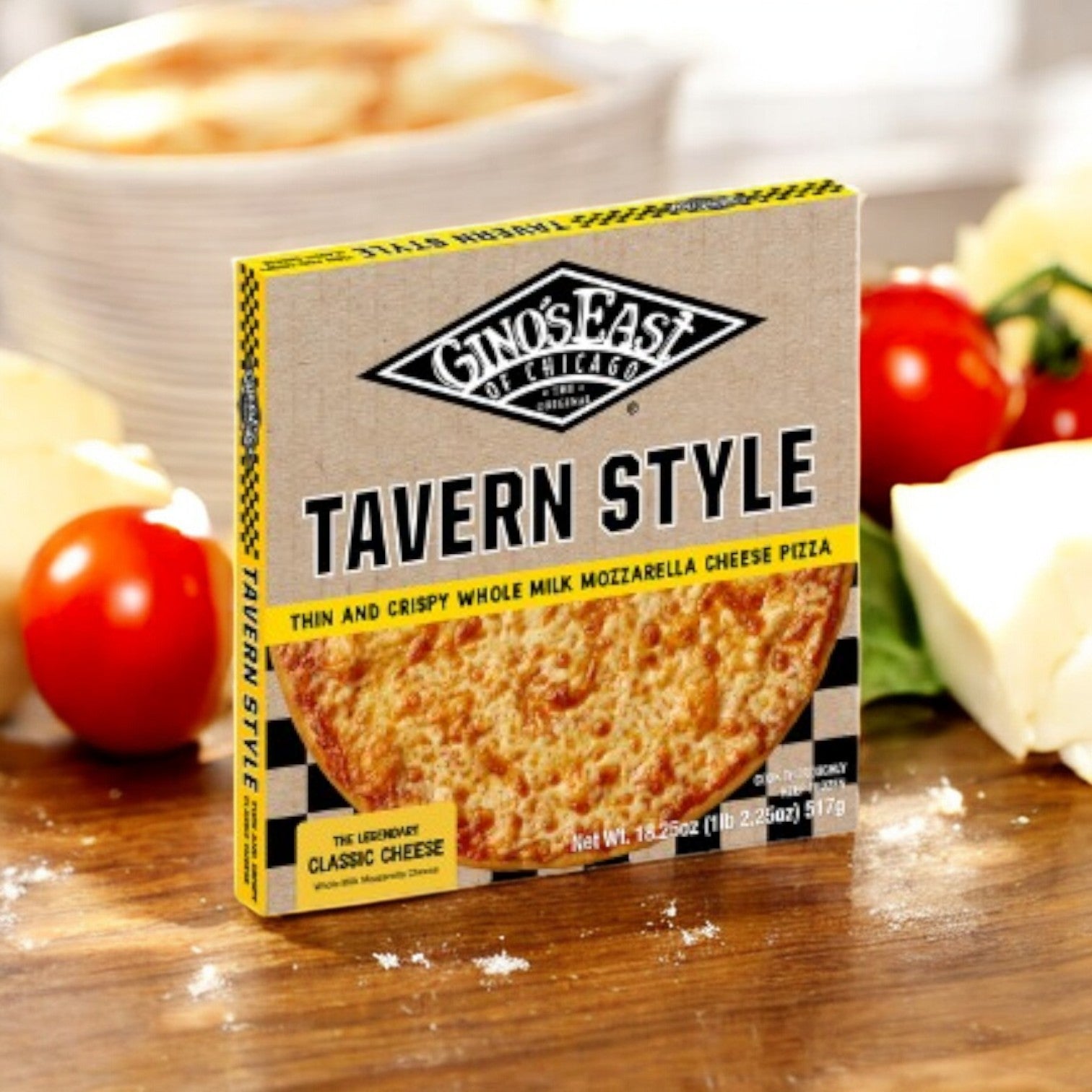 A box of Gino's East Pizza Tavern Style Combo 4 Pack sits on a wooden surface with tomatoes and cheese in the background.