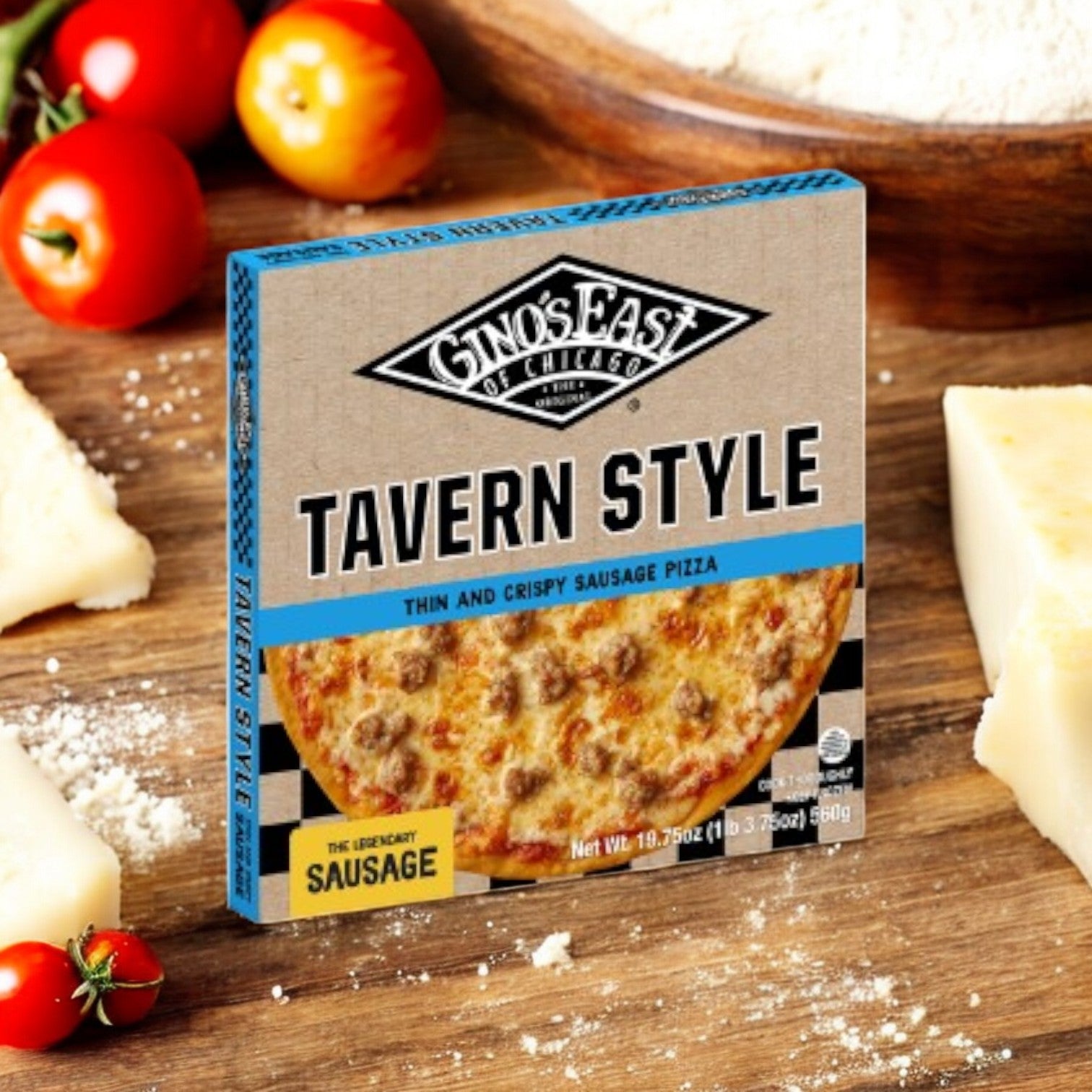 A Gino's East Tavern Style Combo 4 Pack from Gino's East Pizza sits enticingly on a wooden surface, surrounded by cheese blocks, ripe tomatoes, and scattered flour.