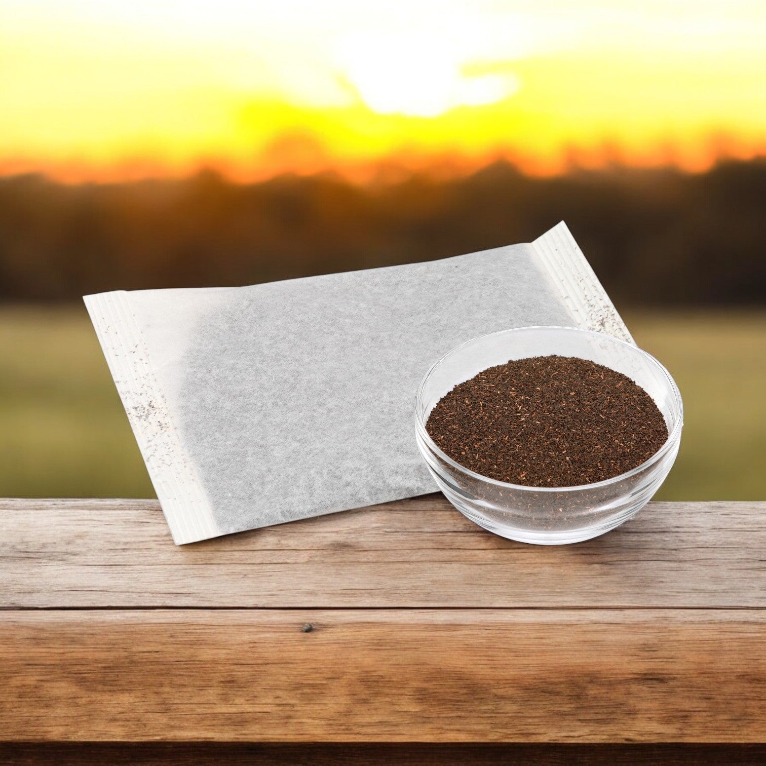 On a wooden surface with a sunset backdrop, a tea bag and loose leaves set the mood for refreshing Tazo Tea Iced Black - 20/1 Gallon. Perfect for breathing life into serene evenings.