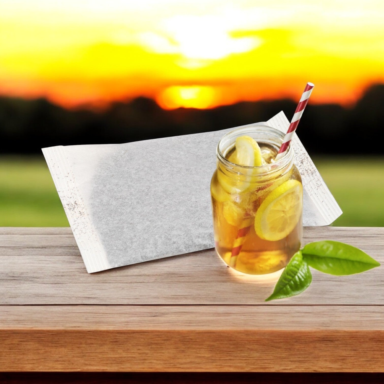 A jar of Tazo Tea Iced Black - 20/1 Gallon with lemon slices and a striped straw sits on a wooden table beside a tea bag. The peaceful scene is enhanced by a sunset over a grassy field.