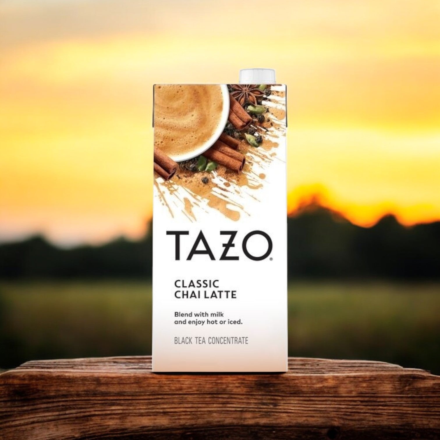 Tazo's Chai Classic Concentrate - 6/32 oz cartons rest elegantly on a wooden surface, illuminated by sunset hues. The blend of black tea inside offers an indulgent experience with every sip.