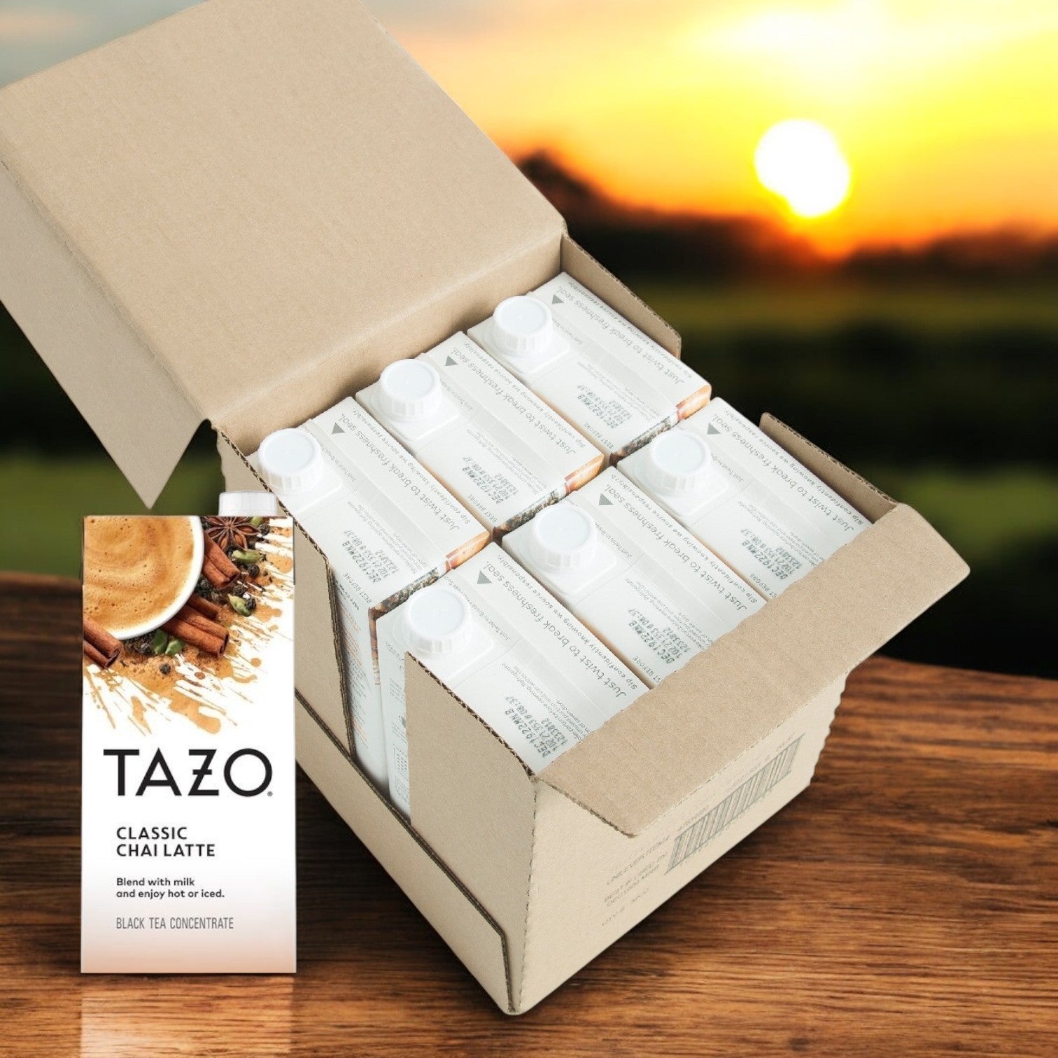A box of Tazo Tea Chai Classic Concentrate - 6/32 oz rests open on a wooden table, displaying the rich blend of black tea as the warm glow of sunset envelops the scene in a cozy ambiance.