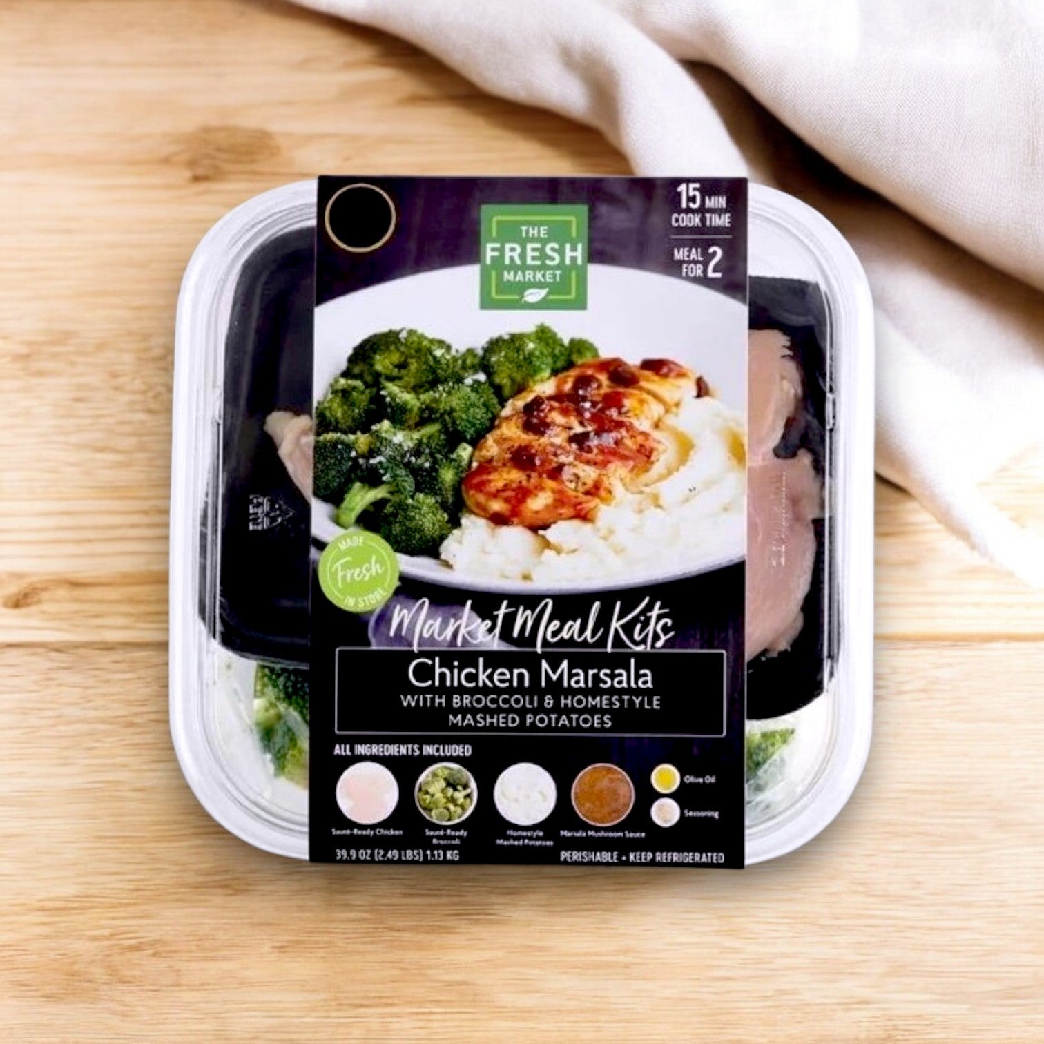 A 39 oz. Market Meal Kit of The Fresh Market's Chicken Marsala with Broccoli & Homestyle Mashed Potatoes rests on a wooden surface.