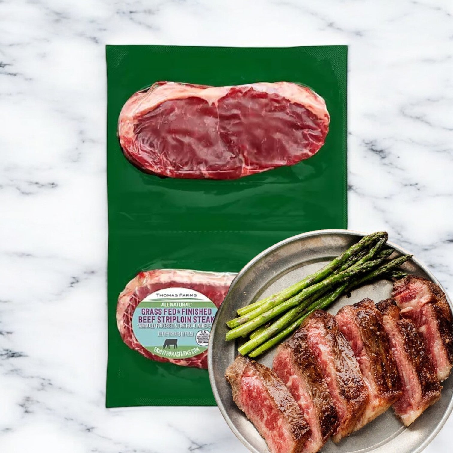 Thomas Farms New York Strip Steak, featuring two premium grass-fed steaks from Thomas Farms, is displayed next to a plate with sliced cooked steak and asparagus on a marble background, highlighting its exceptional quality.