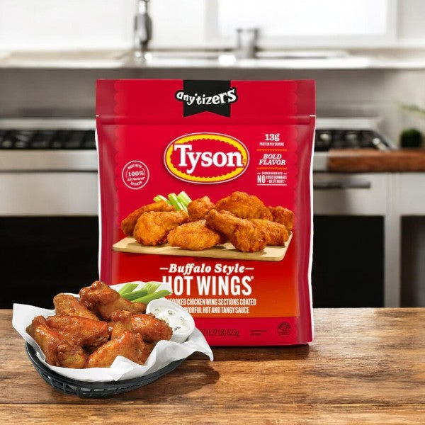 A Tyson Any’tizers Frozen Bone-In Buffalo Style Hot Wings Bag (1.37 lbs) rests on a table near a basket of sauced wings, each bite offering a burst of spicy flavor.