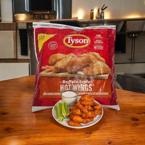 A bag of Tyson Buffalo Style Hot Wings, Fully Cooked Chicken Wing, 4lbs. sits beside a plate of these wings with celery sticks and ranch dip on a rustic wooden table in a kitchen setting.