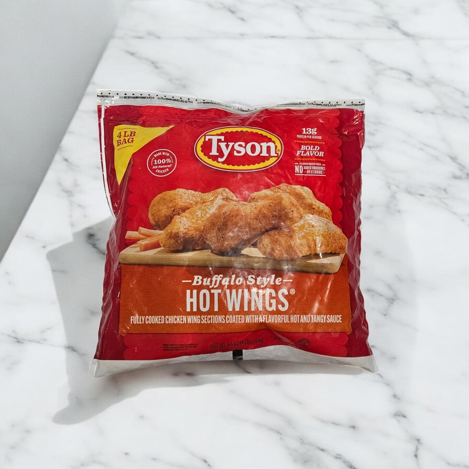 A 4lb. bag of Tyson Buffalo Style Hot Wings is on a marble surface, showcasing its vibrant red packaging with an enticing image of perfectly glazed Buffalo sauce wings.