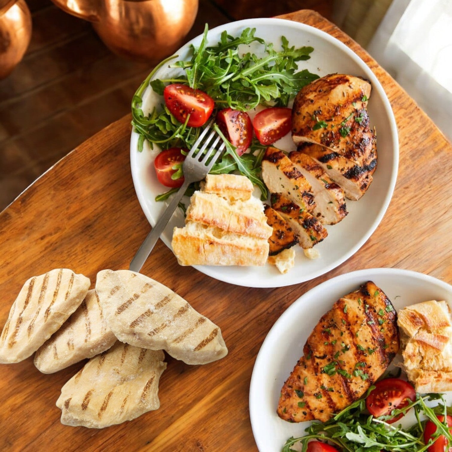 Two plates of Tyson Red Label Grilled Chicken Breast with cherry tomatoes and arugula offer a high-protein meal, served with grilled flatbreads on the side.