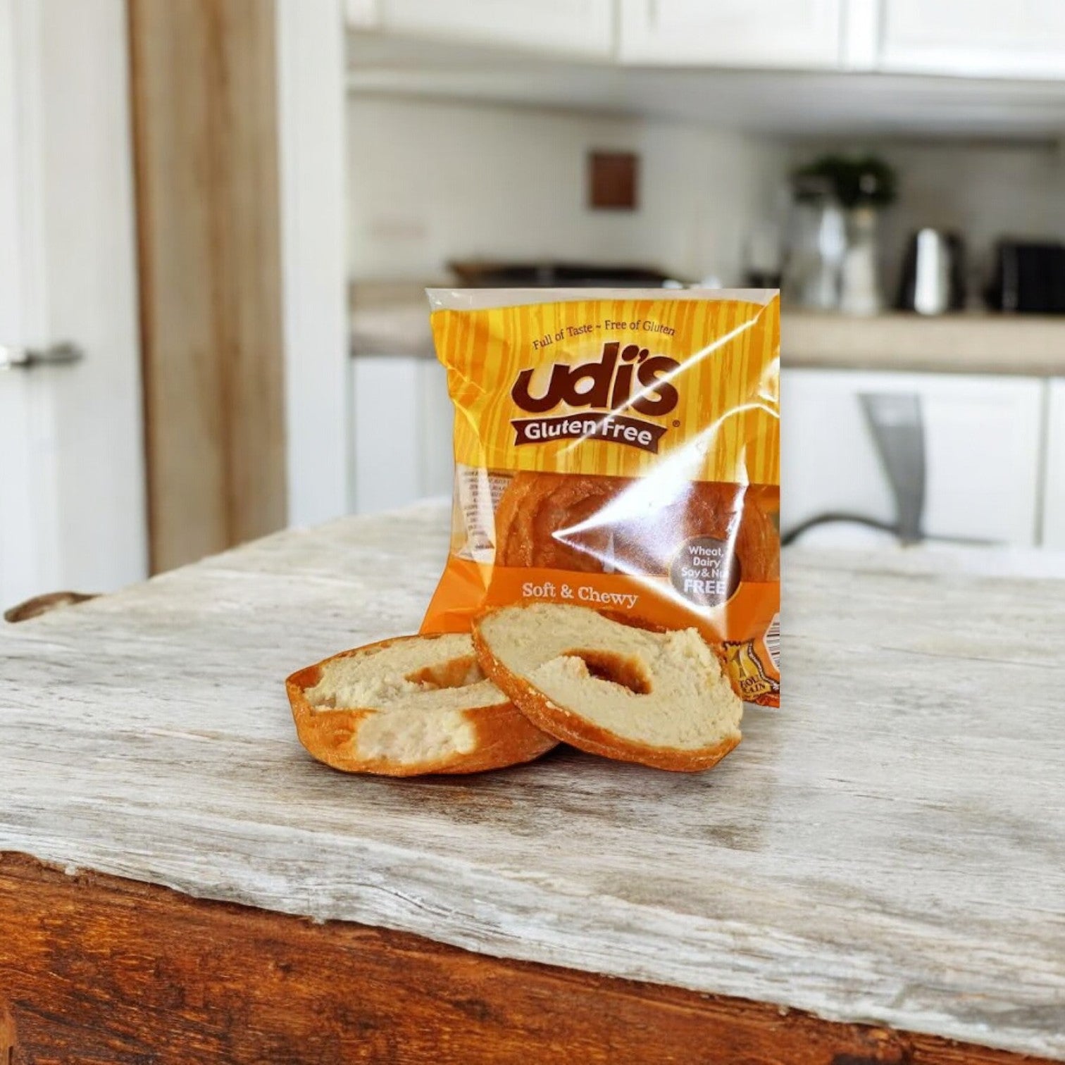 An open package of Udi's Plain Bagel, 3.5 oz., rests on a wooden table. Two half bagels showcase their tempting gluten-free appeal, highlighting Udi's renowned classic flavor and texture.